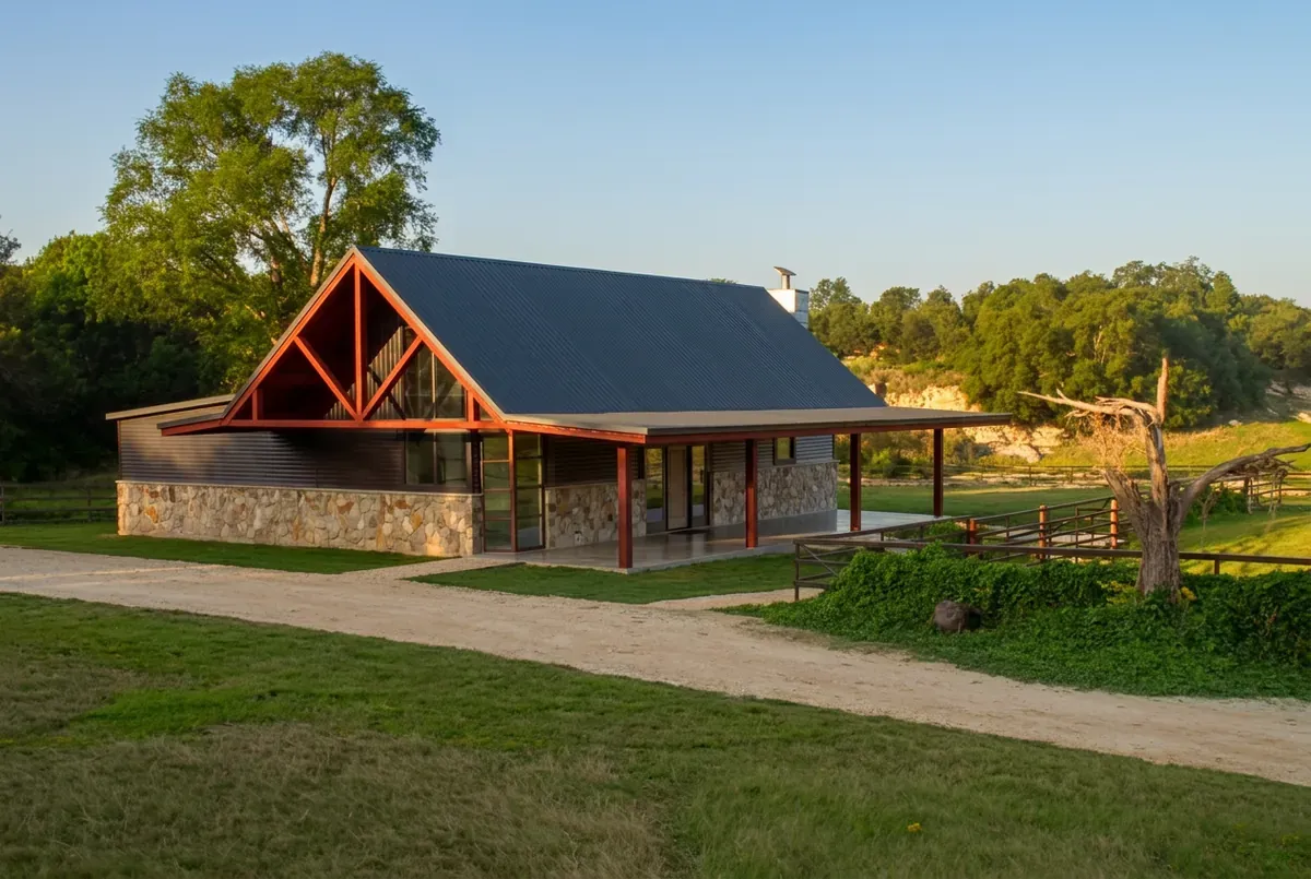 A steel-framed metal building home with a red-iron gable, stone wainscot, and standing-seam roof in the Texas Hill Country