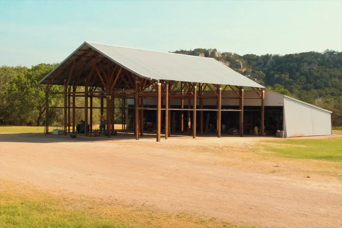 A large open post-frame pole barn for equipment against a Hill Country limestone bluff
