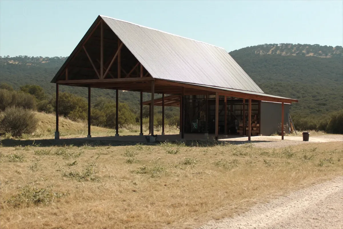 A post-frame pole barn with an open bay and an enclosed end on Texas Hill Country ranch land