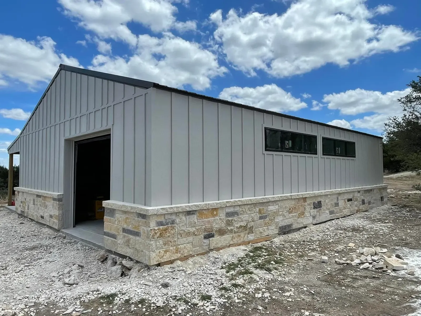 A gray board-and-batten steel building with a limestone wainscot and clerestory windows in Texas