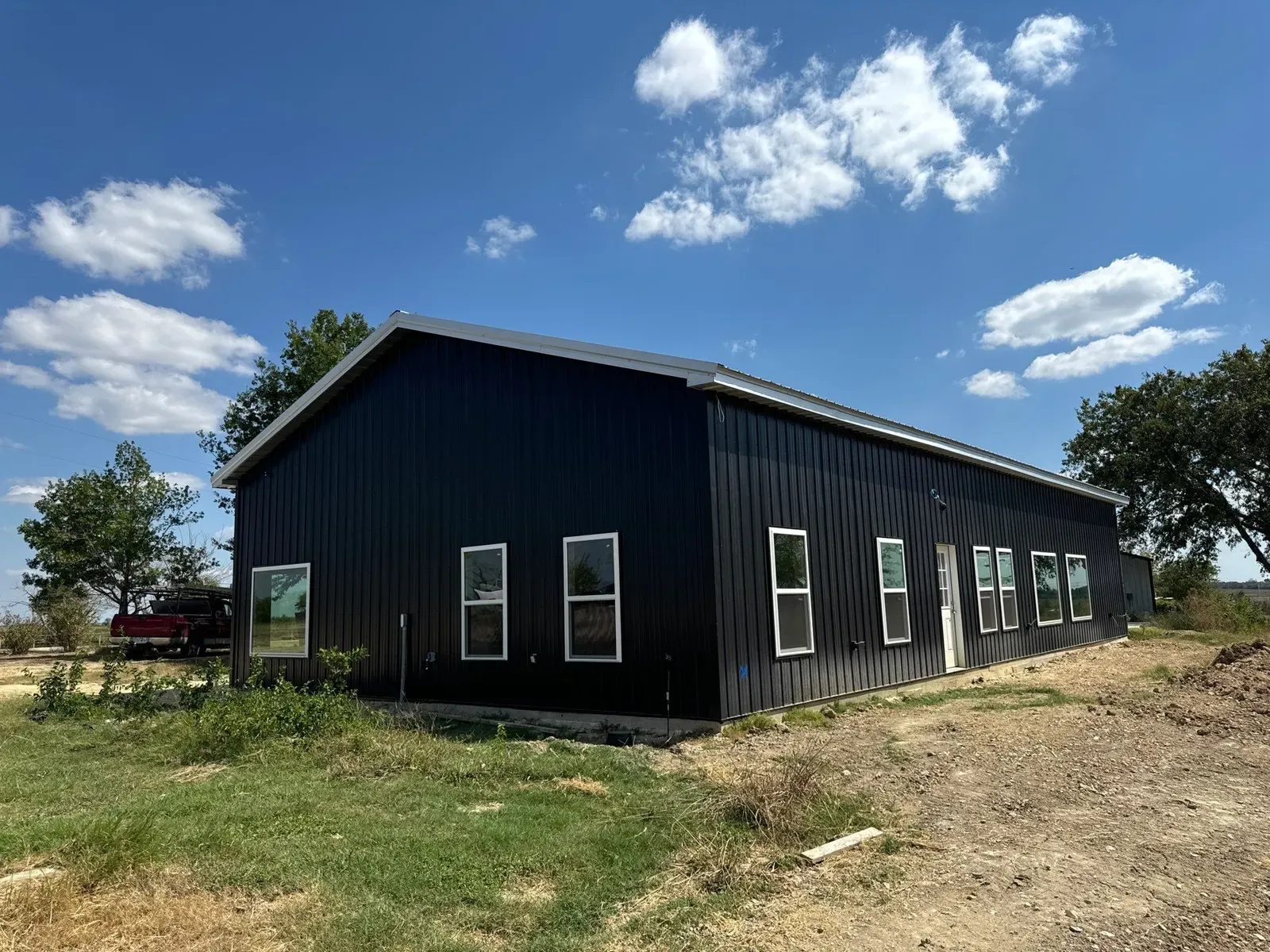 A long black steel barndominium with a row of white-framed windows on open land in Texas
