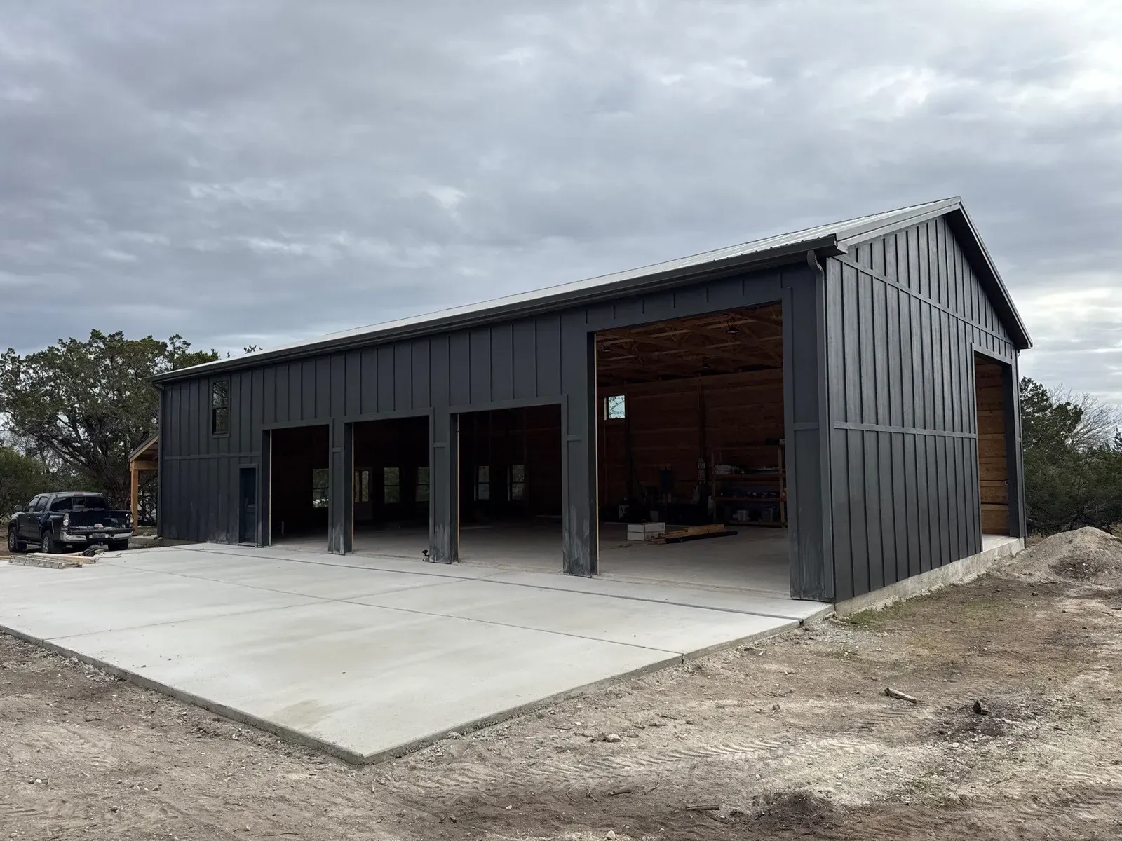 A charcoal board-and-batten steel shop with four large bays and a wide concrete apron in Texas