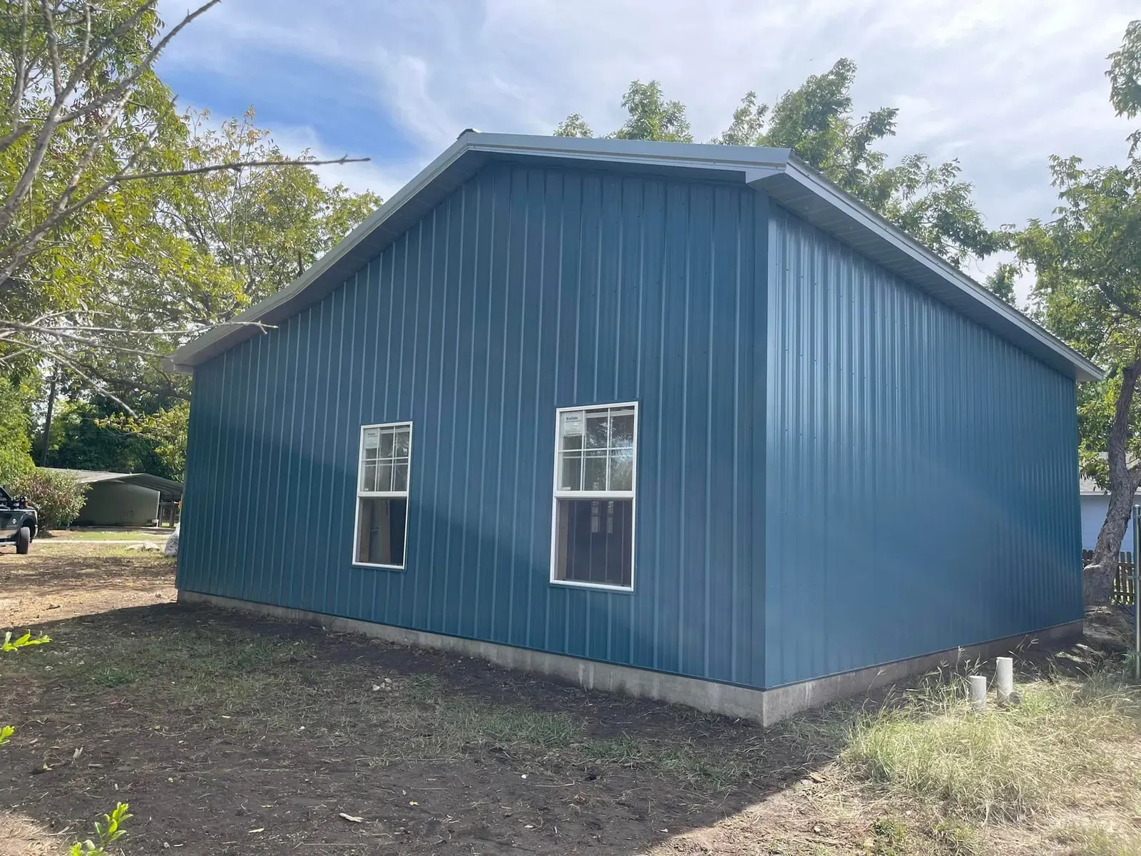 A small blue steel building with two white-framed windows among trees in Texas