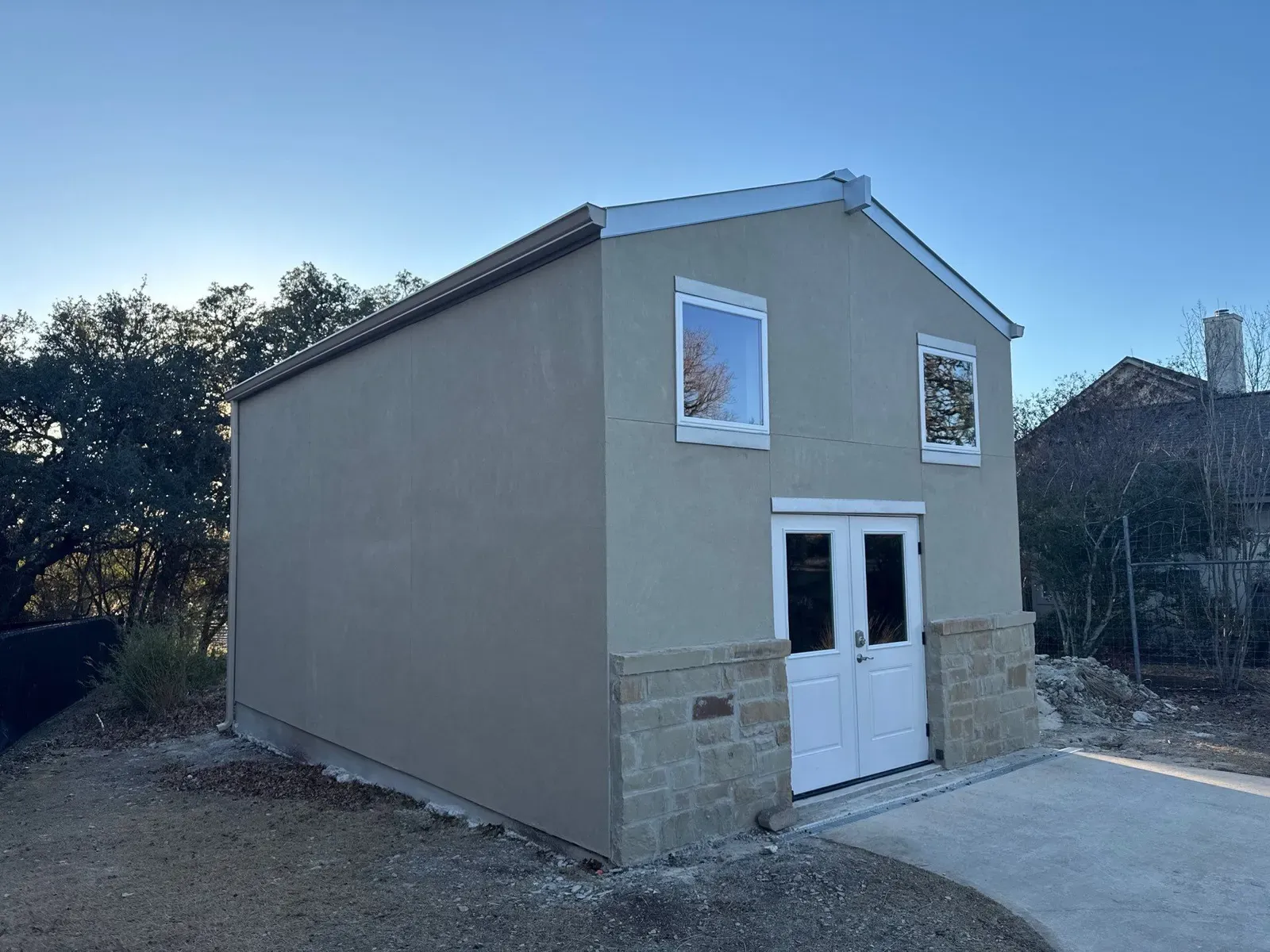 A two-story steel building with a stucco finish, stone wainscot and white French doors in Texas