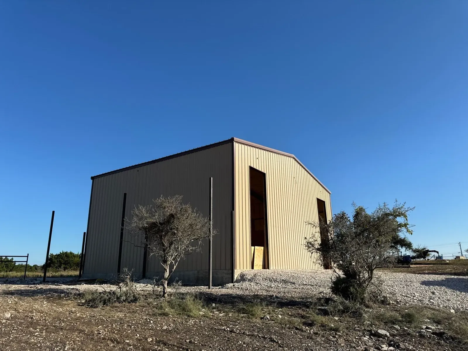 A tall tan steel building with framed openings on a gravel pad in Texas