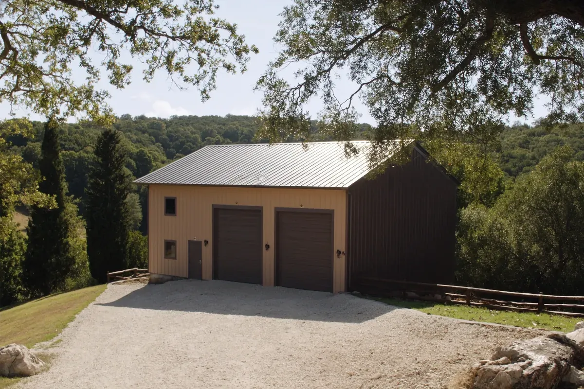 A metal garage and shop building on a gravel pad in the wooded Texas Hill Country